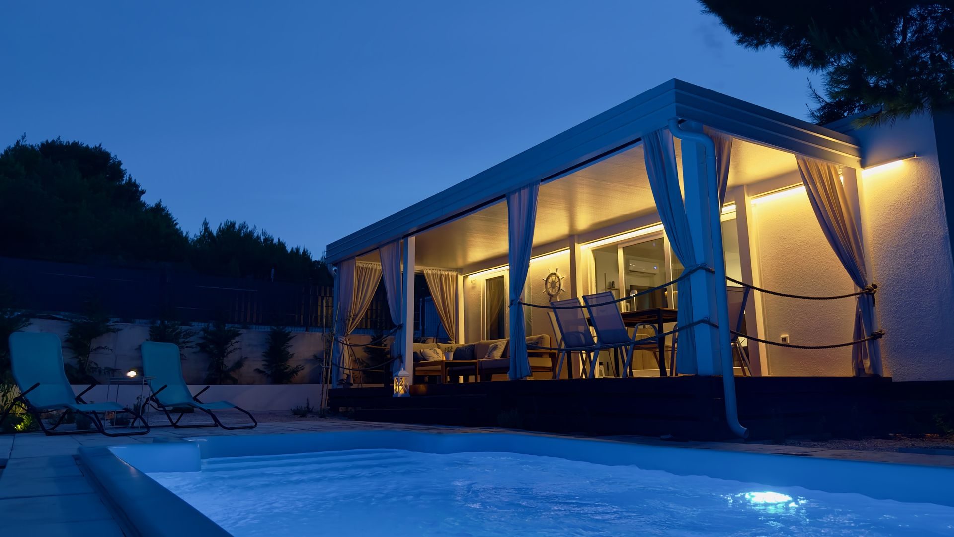 Private pool of a Salvia home lit at night, with the covered terrace behind it
