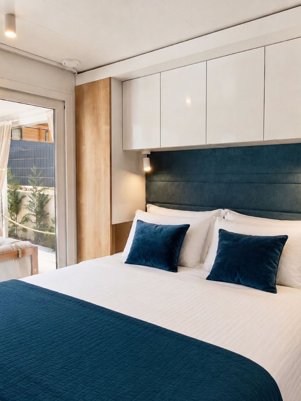 Modern master bedroom with dark blue upholstered headboard, white bedding, and sliding glass door to a private patio at Salvia Beachside Homes