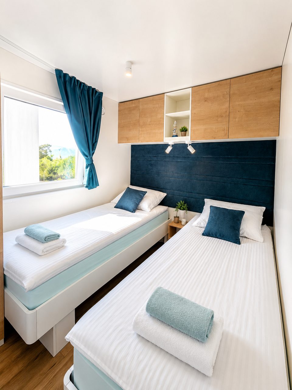 Bright modern twin bedroom with two single beds, white and light blue bedding, dark blue headboard, and wooden cabinets at Salvia Beachside Homes
