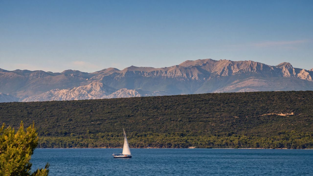 View across the Adriatic Sea towards the Velebit mountains, with a sailboat in the foreground
